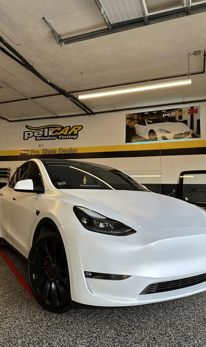 White Tesla Model Y in a garage with tinted windows and a clean exterior.